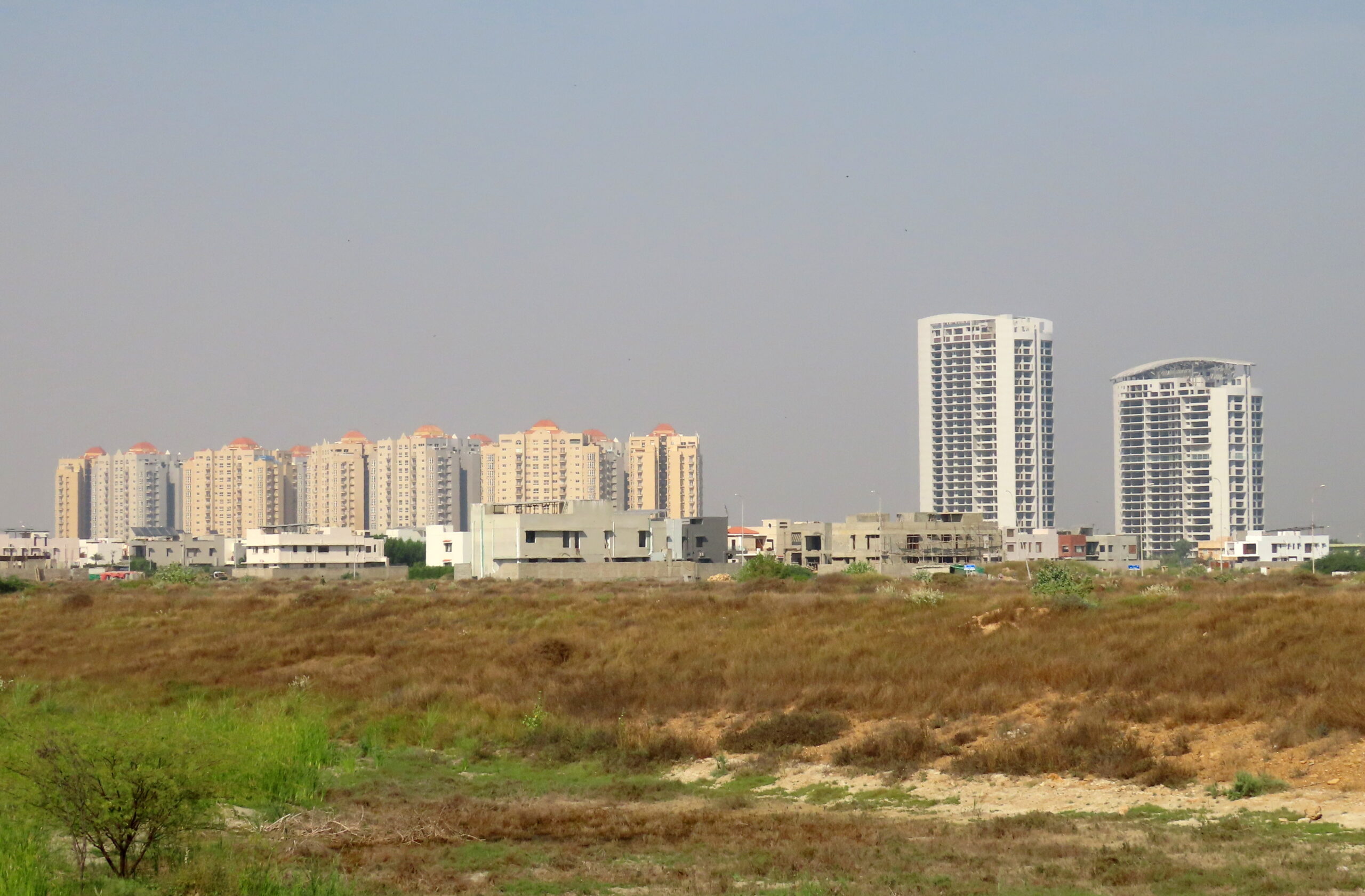 Apartment towers rise beyond open land in DHA Phase 8, Karachi, in December 2022