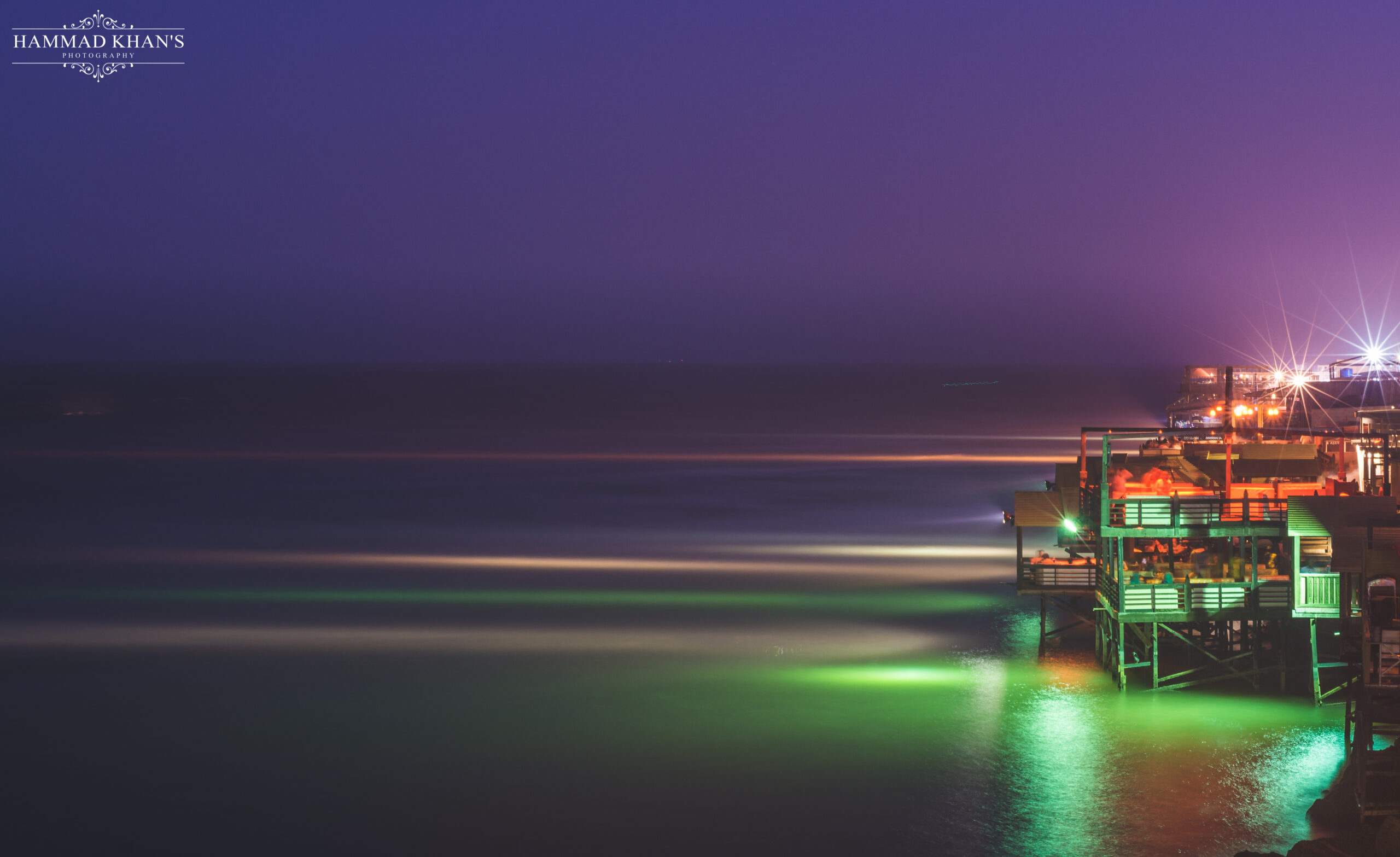 Lit restaurant decks at Do Darya stand over the Arabian Sea at blue hour