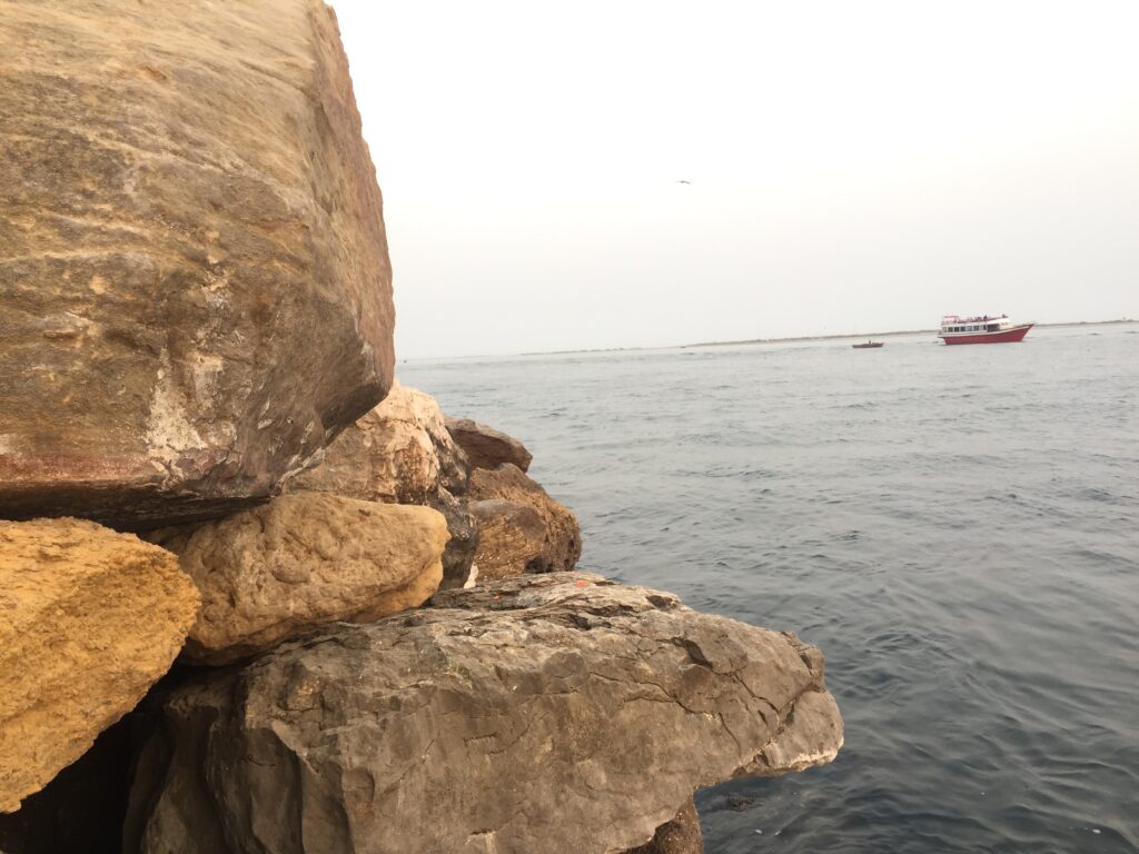 Sandstone boulders meet the sea at Do Darya, with a small boat on the water
