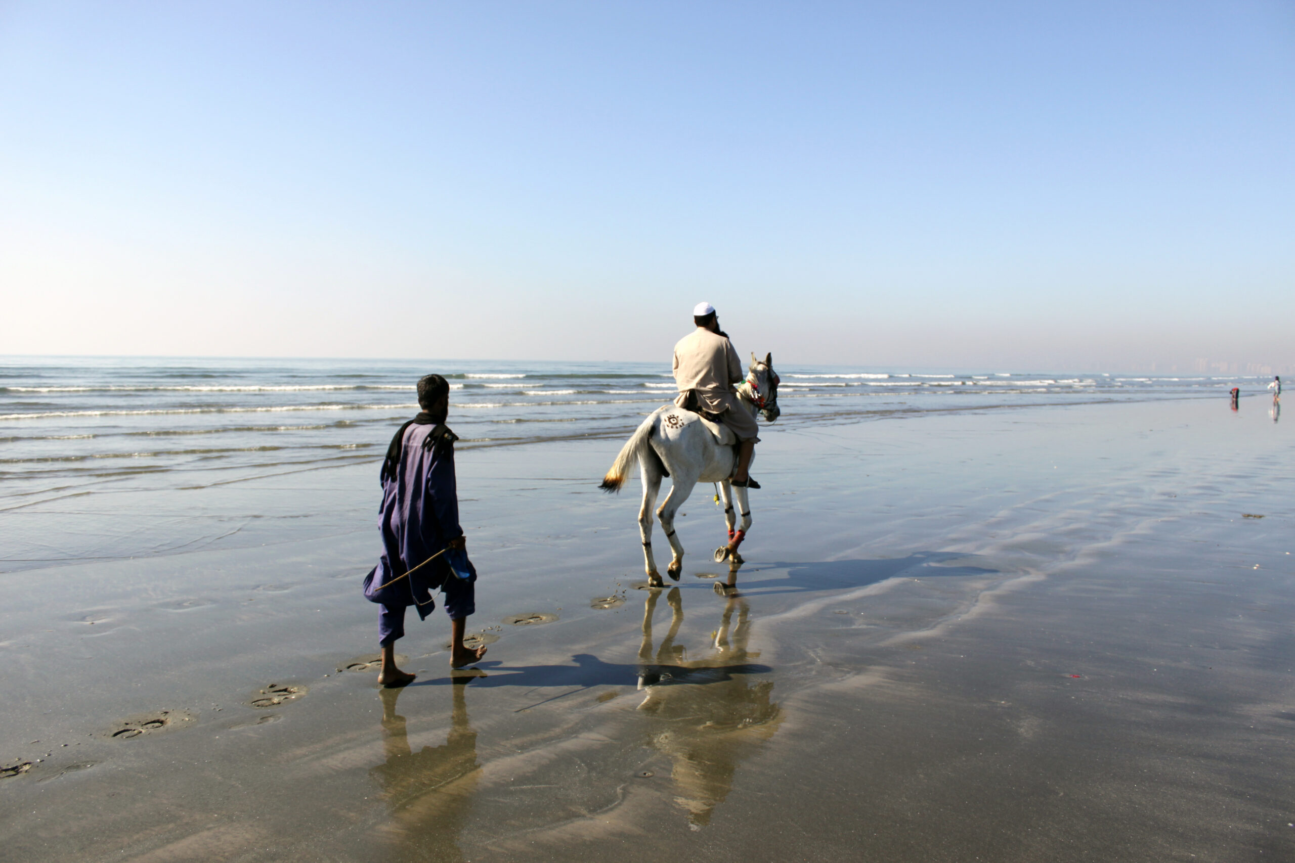 A horse rider and a walker cross the wet sand at Sea View, Clifton